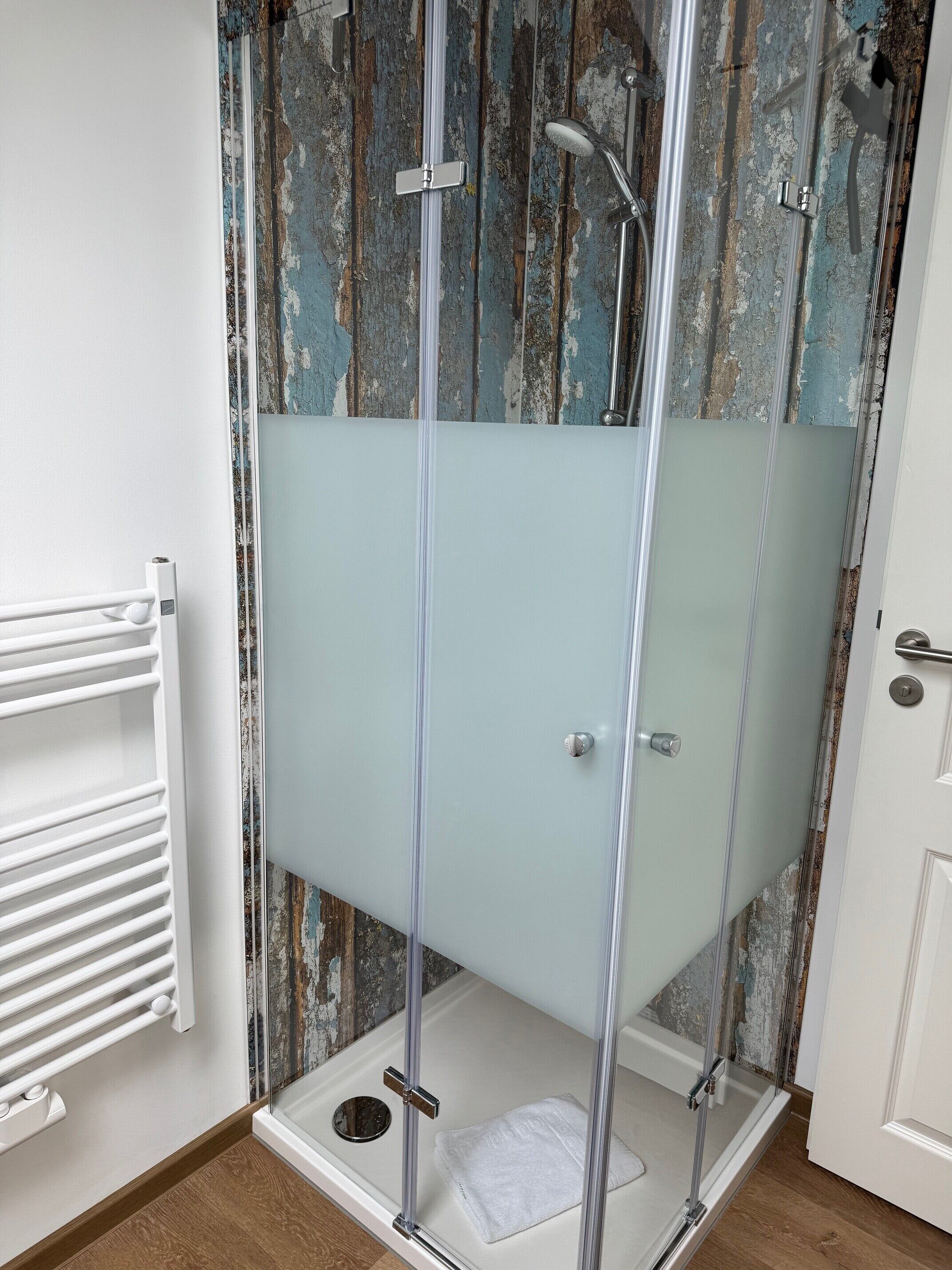 A glass-enclosed shower with a white towel, a white radiator, and a rustic wall.