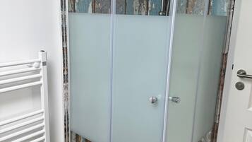 A glass-enclosed shower with a white towel, a white radiator, and a rustic wall.