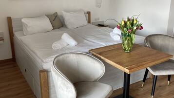 A bedroom with a bed, a wooden table, two chairs, a vase with flowers, and a painting on the wall.