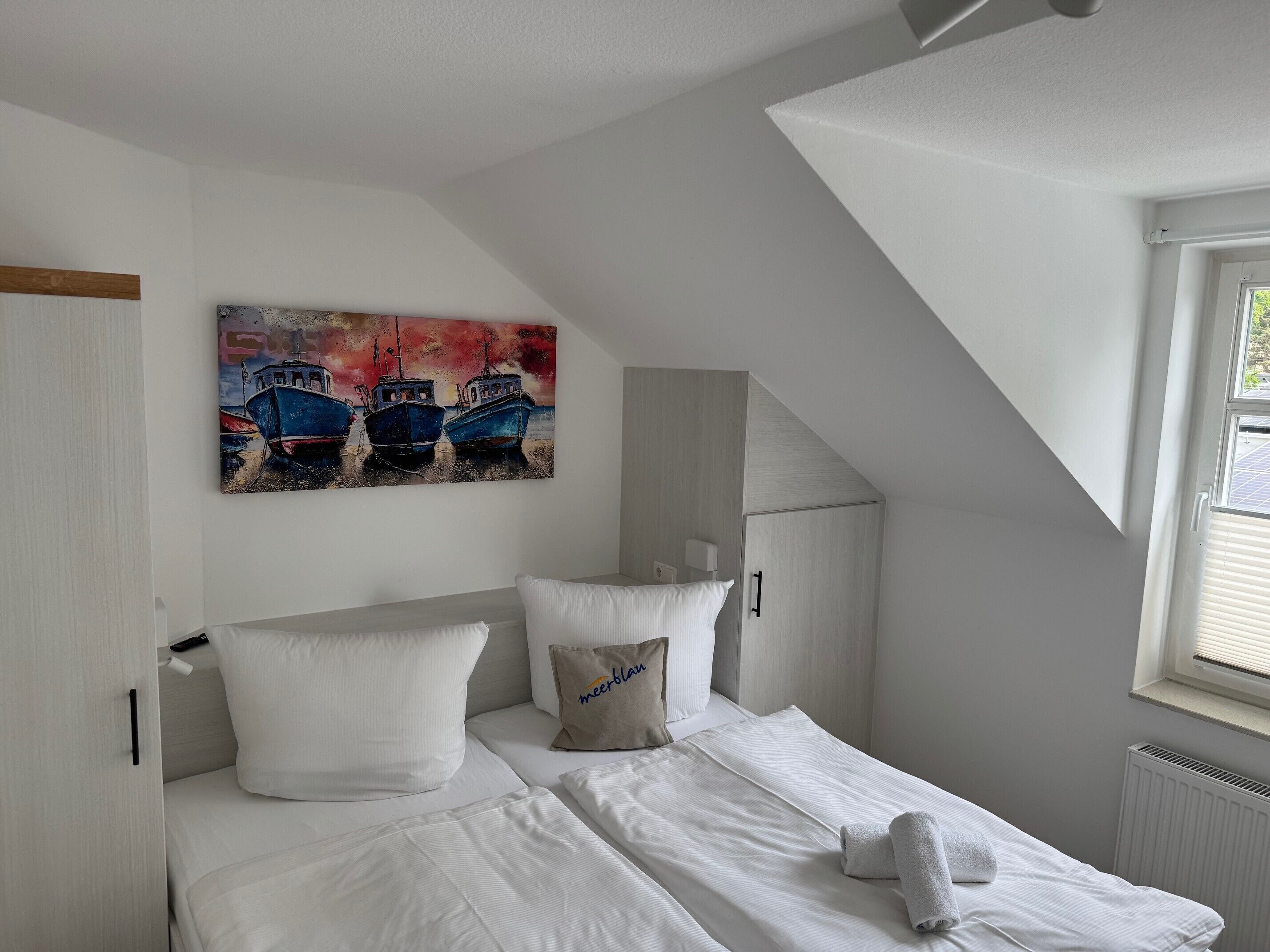 A bedroom with a bed, pillows, a painting, a window, and a radiator.