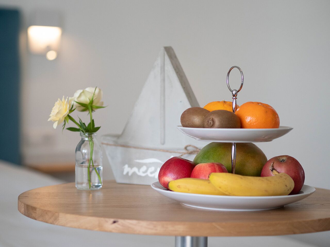 A wooden table with a fruit arrangement and a vase of white flowers.