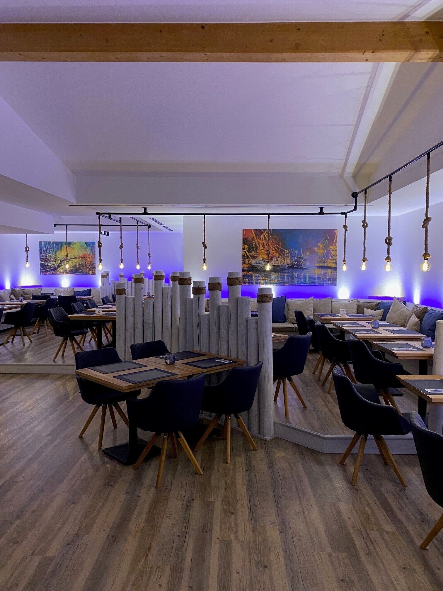 A modern restaurant with wooden tables, black chairs, and hanging light fixtures.
