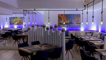 A modern restaurant with wooden tables, black chairs, and hanging light fixtures.