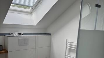 Un baño moderno con tragaluz, inodoro, lavamanos y cabina de ducha de vidrio.
