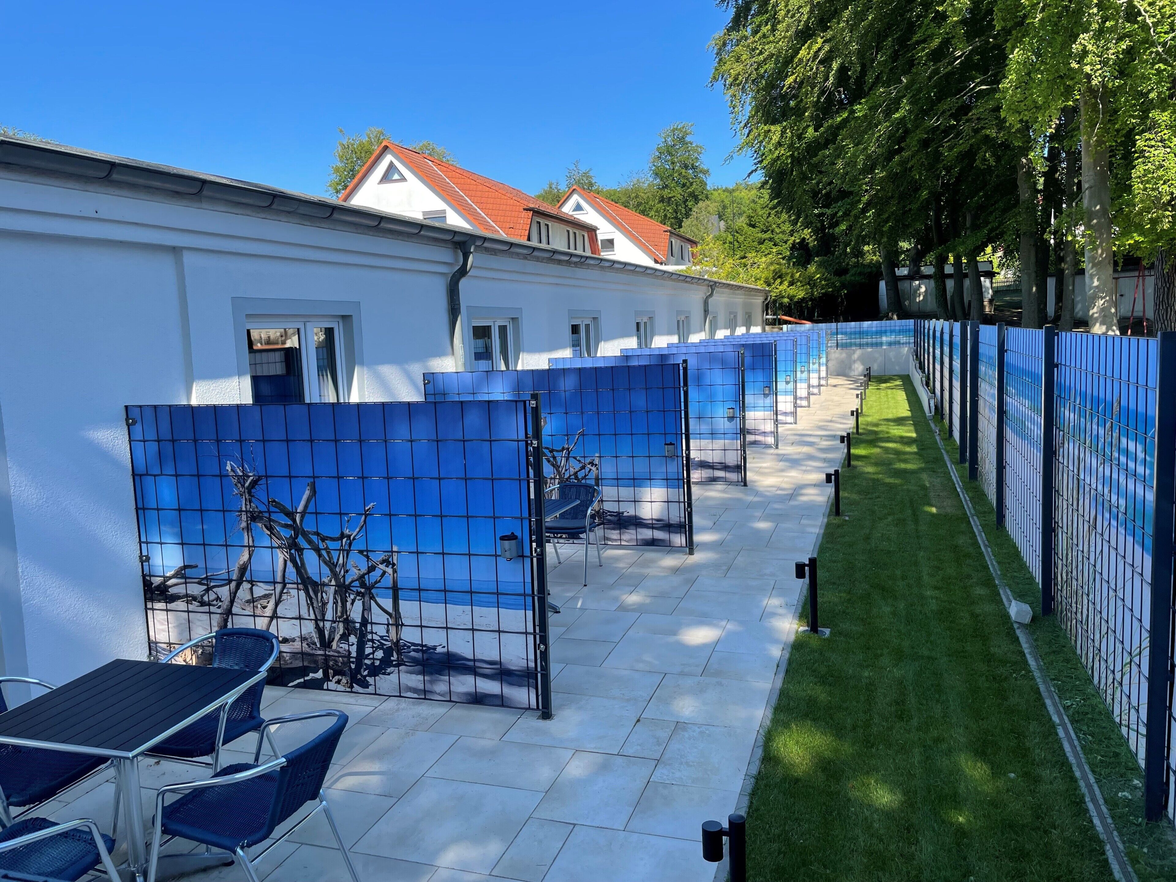 Una fila de habitaciones azules separadas por paneles, con un edificio blanco al fondo.