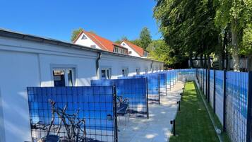Una fila de habitaciones azules separadas por paneles, con un edificio blanco al fondo.