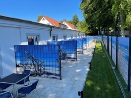 Una fila de habitaciones azules separadas por paneles, con un edificio blanco al fondo.