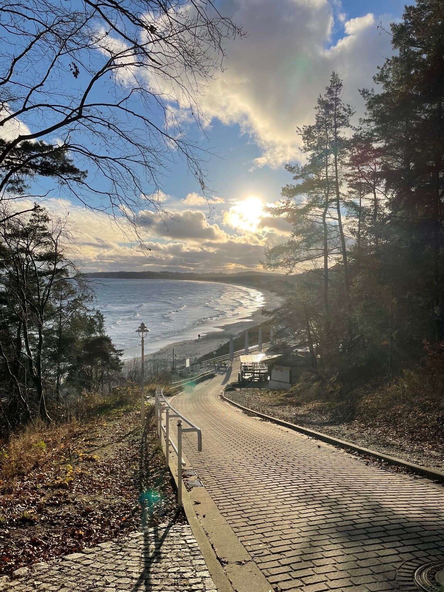 A paved pathway leading to a beach with a view of the ocean and a clear sky.
