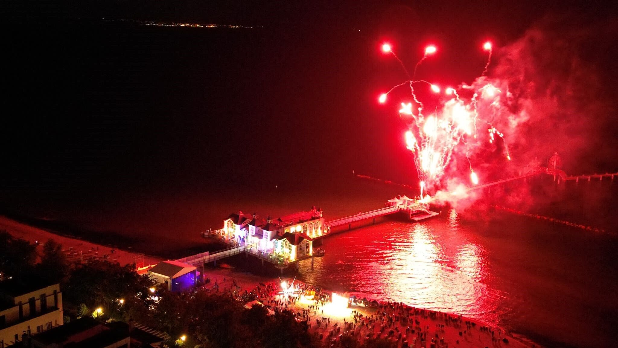 Un hotel frente al agua con un puente, gente y fuegos artificiales.