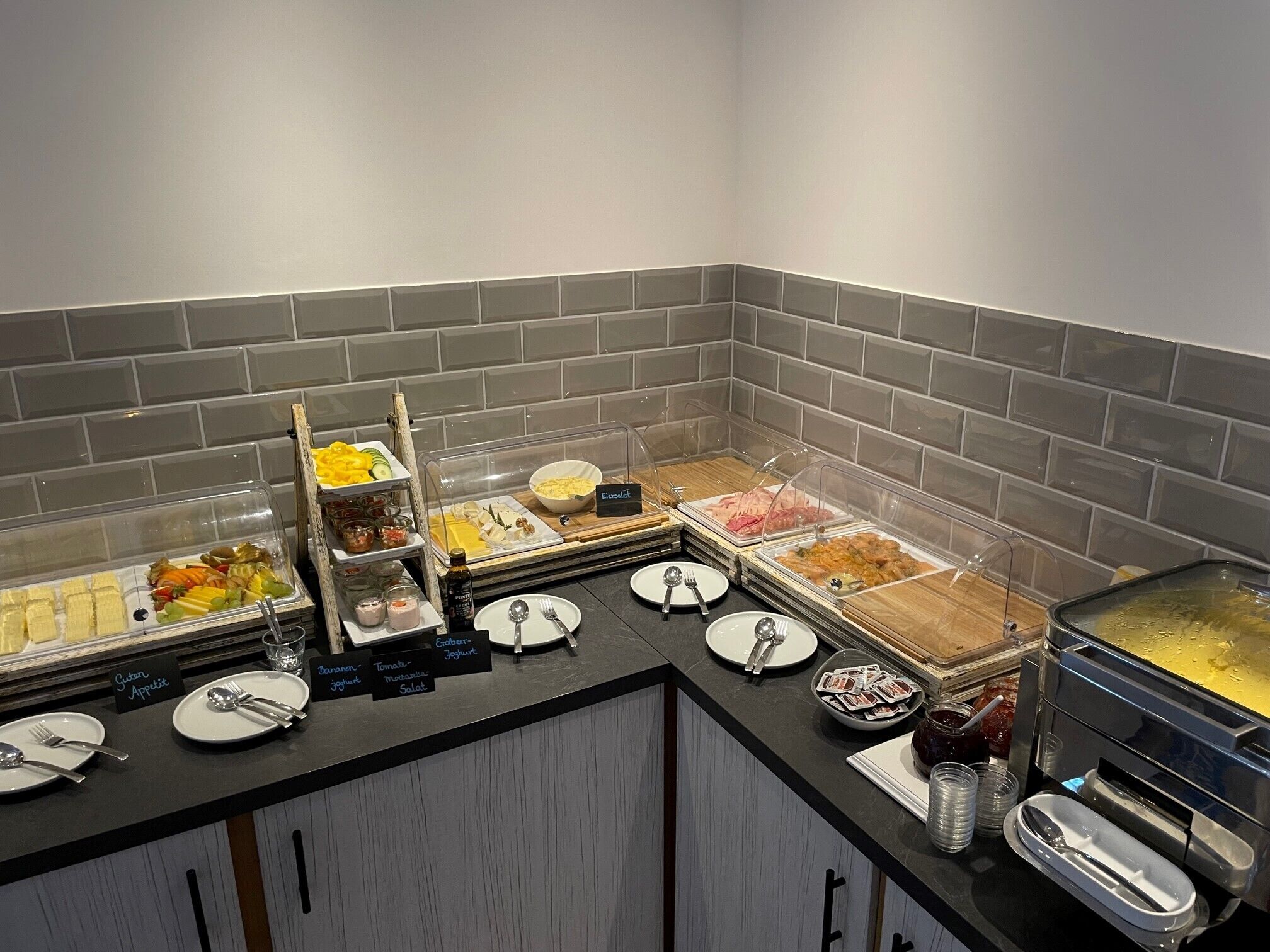 A buffet with various food items and condiments, including fruits, meats, and salads, arranged on a counter with clear serving dishes.