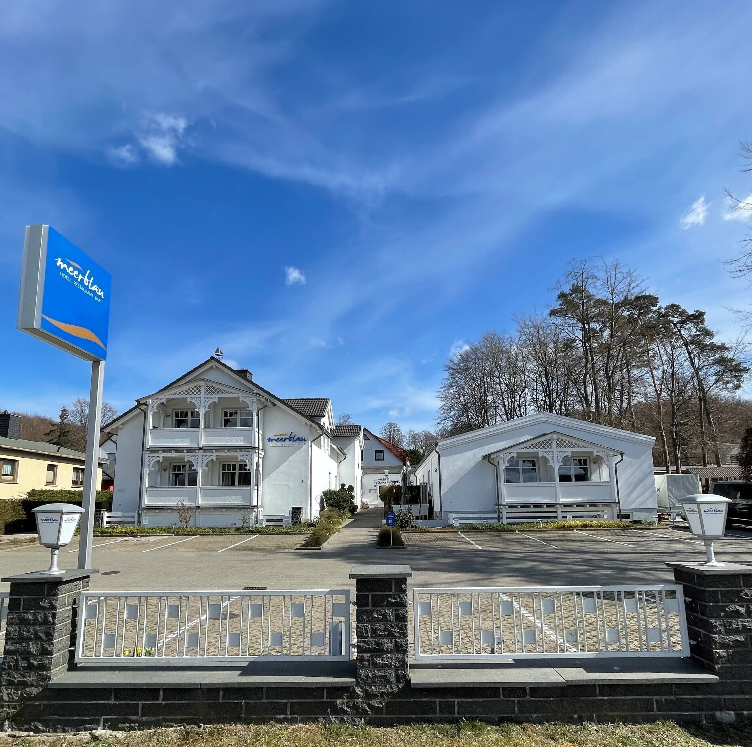 Un hôtel reconnaissable à son panneau « meerblau » bien visible, qui présente un style architectural classique, avec un balcon et une véranda couverte.