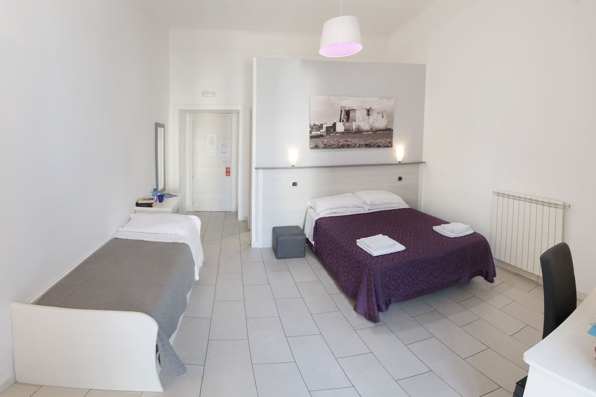 A hotel room with two beds, a desk, a chair, a radiator, and a wall-mounted picture.