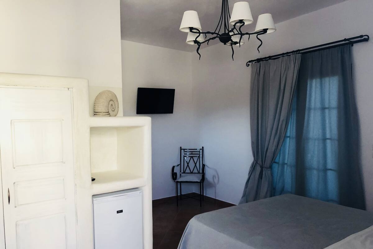 A bedroom with a bed, a small white cabinet, a television on the wall, and a chair.
