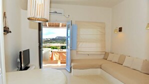 Ein Zimmer mit großem Fenster, einer Couch, einem Fernseher und einer Lampe.