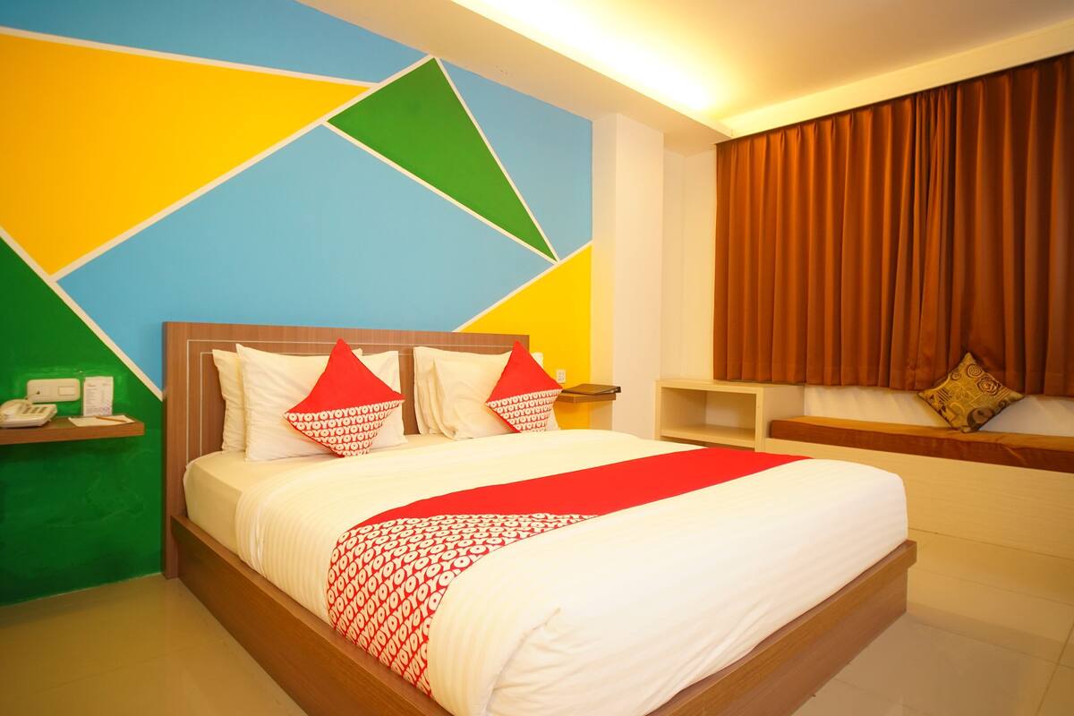 Quarto de hotel com cama, mesa de cabeceira, telefone e parede com padrões geométricos.