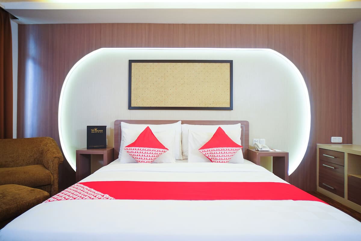 Quarto de hotel com uma cama grande, duas almofadas, uma mesinha de cabeceira, uma cadeira e um quadro na parede.