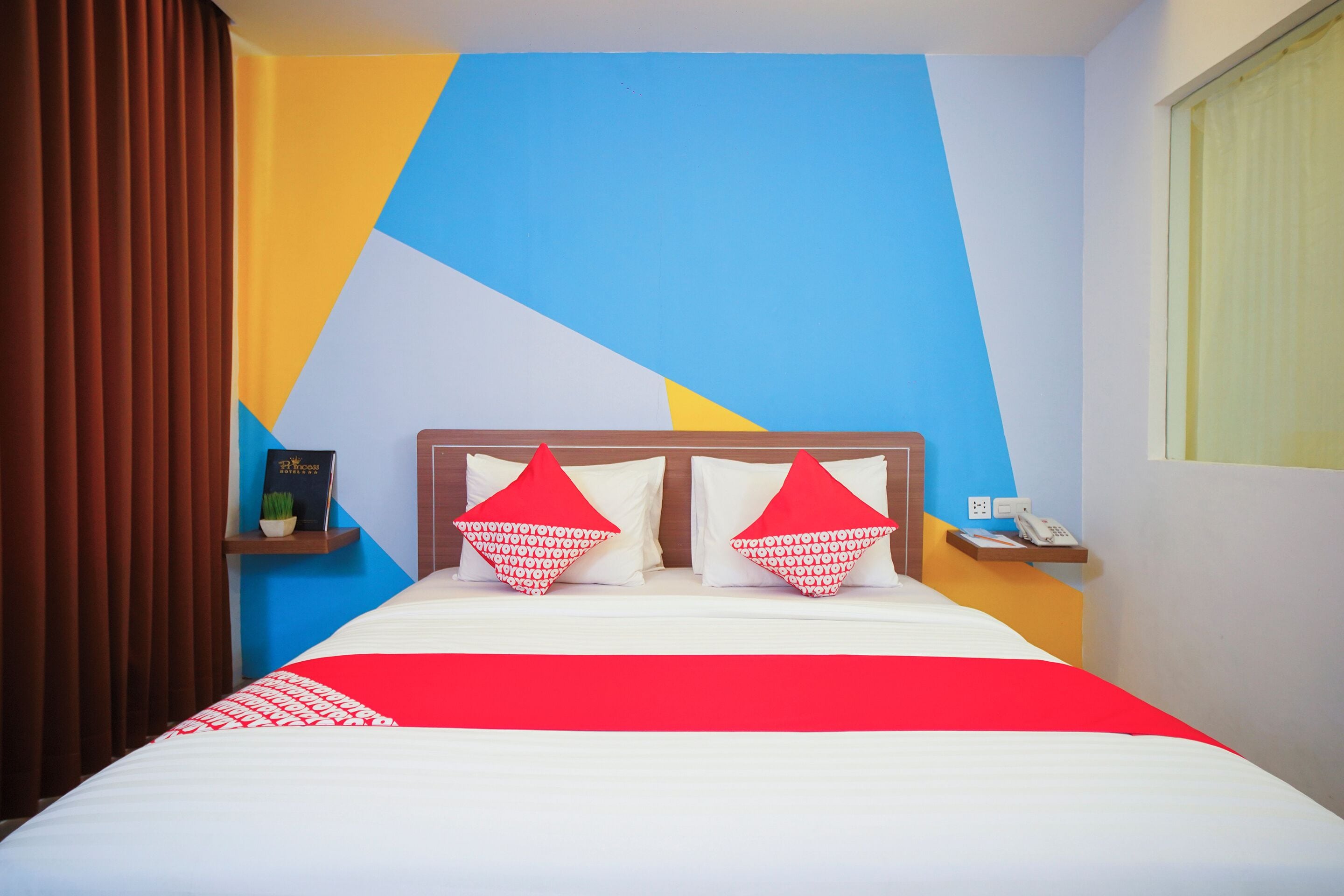 A hotel room with a bed, pillows, a nightstand, a phone, and a wall with geometric patterns.