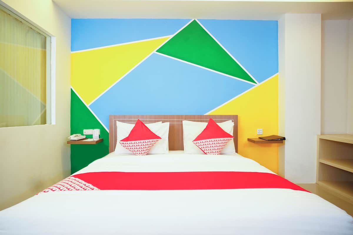 Quarto de hotel com cama, mesa de cabeceira, cortinas e parede com padrões geométricos.