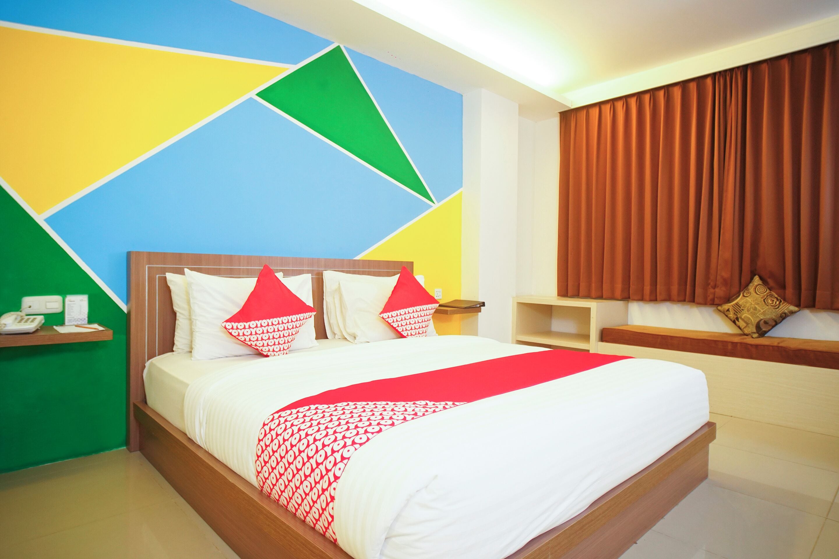 A hotel room with a bed, a nightstand, a wall clock, and a window with curtains.