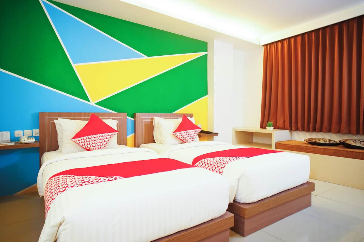 Quarto de hotel moderno com duas camas, design geométrico na parede e vista para a cidade.