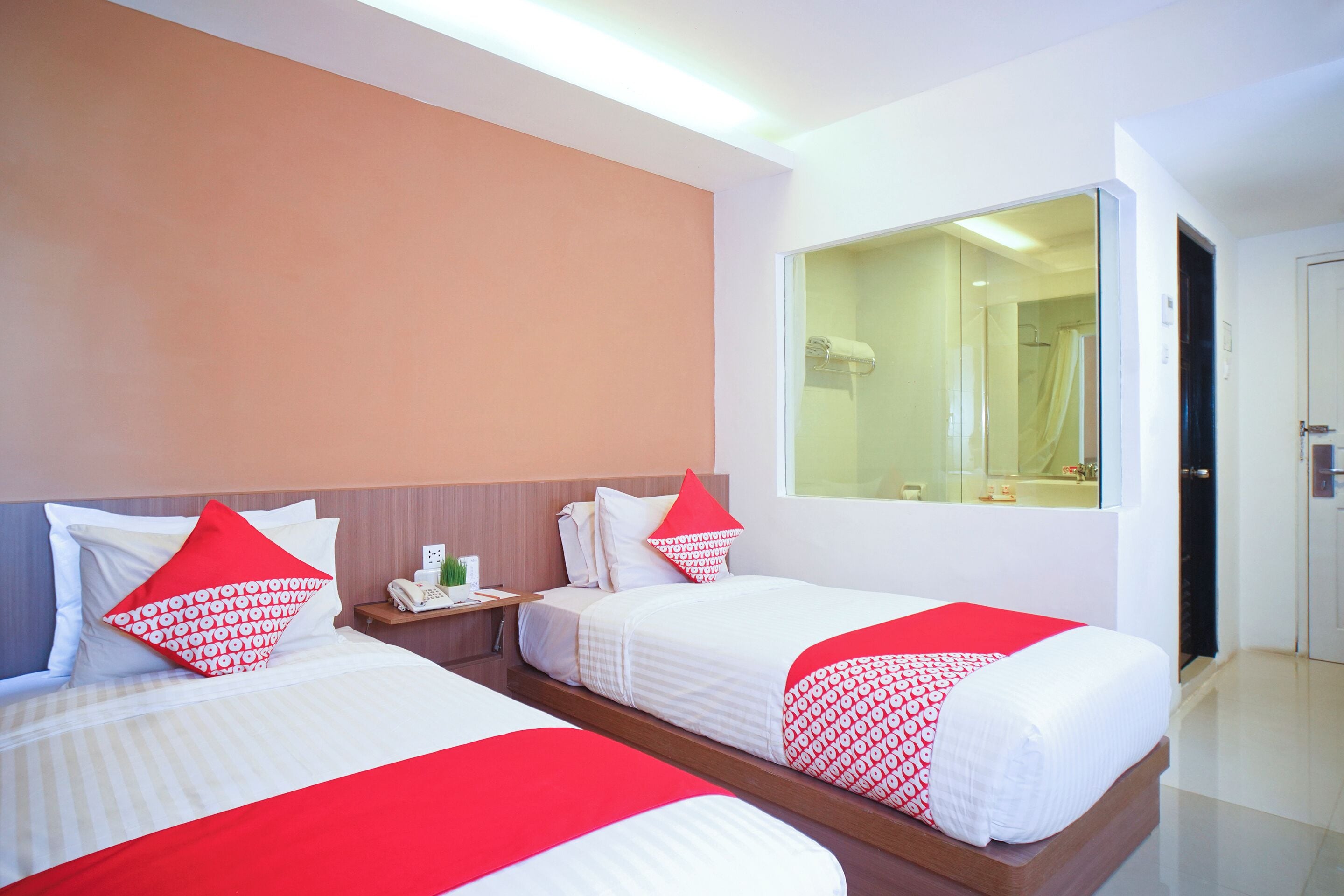 A hotel room with two beds, each with red and white bedding, a nightstand with a phone, and a large mirror on the wall.