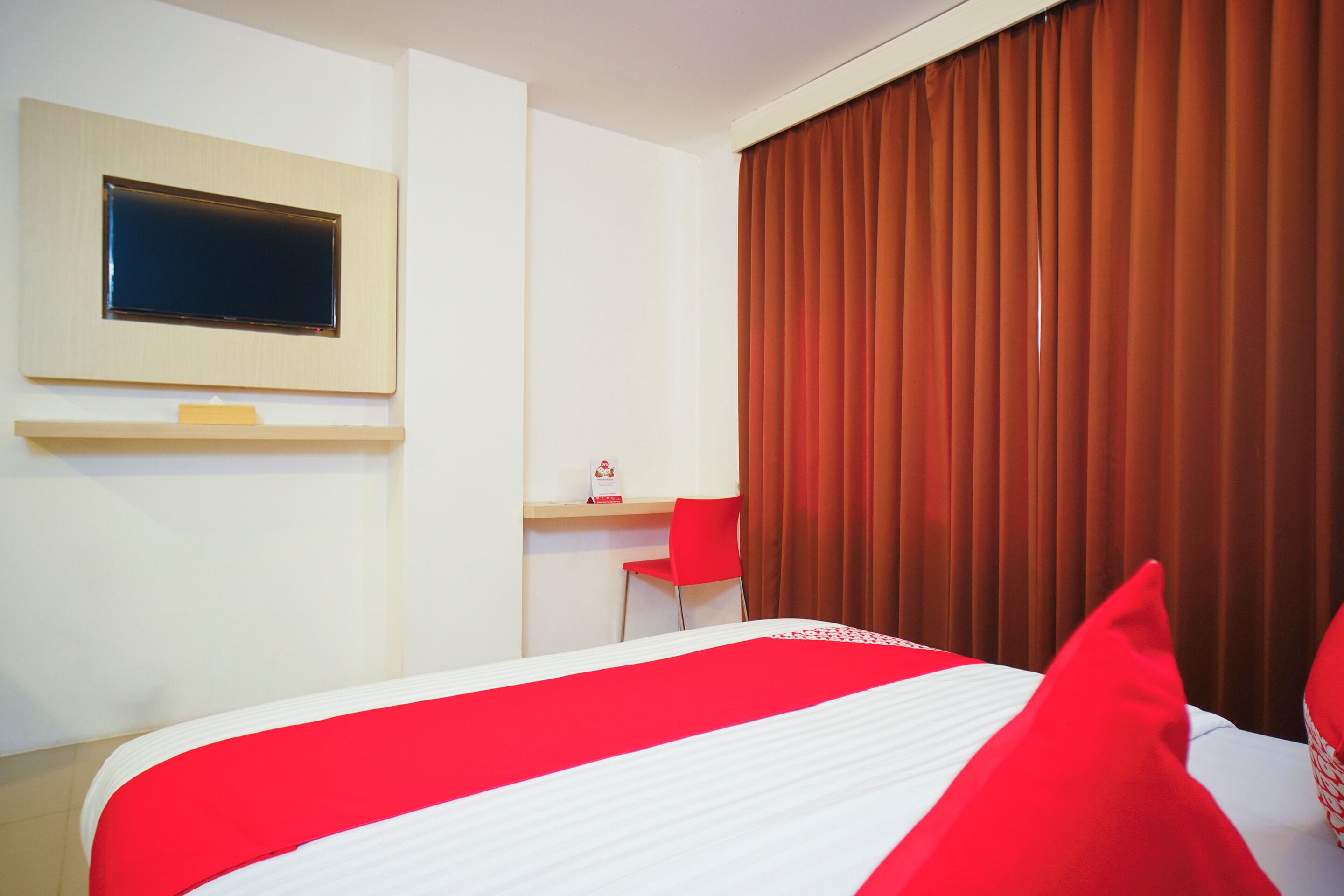 Una habitación de hotel con cama, escritorio, silla, televisor y ventana con cortinas.