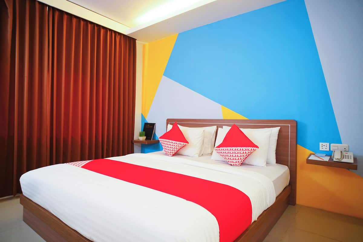 Quarto de hotel com uma cama grande, roupa de cama vermelha e branca, e um design geométrico na parede.
