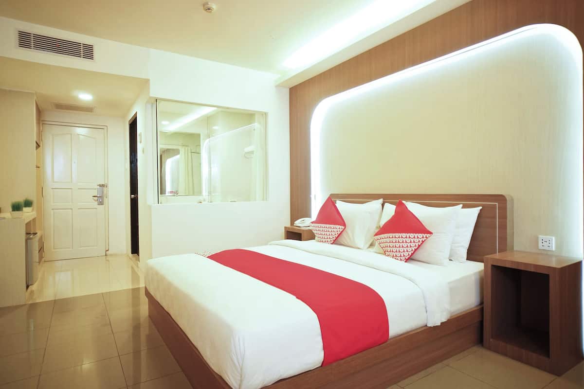 Quarto de hotel com uma cama grande, uma mesinha de cabeceira, um espelho e uma porta que dá para o banheiro.