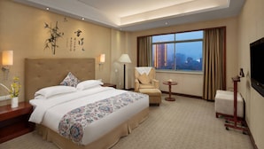 A hotel room with a large bed, a chair, a small table, and a TV. - Yiyang Huatian Hotel (Yiyang)