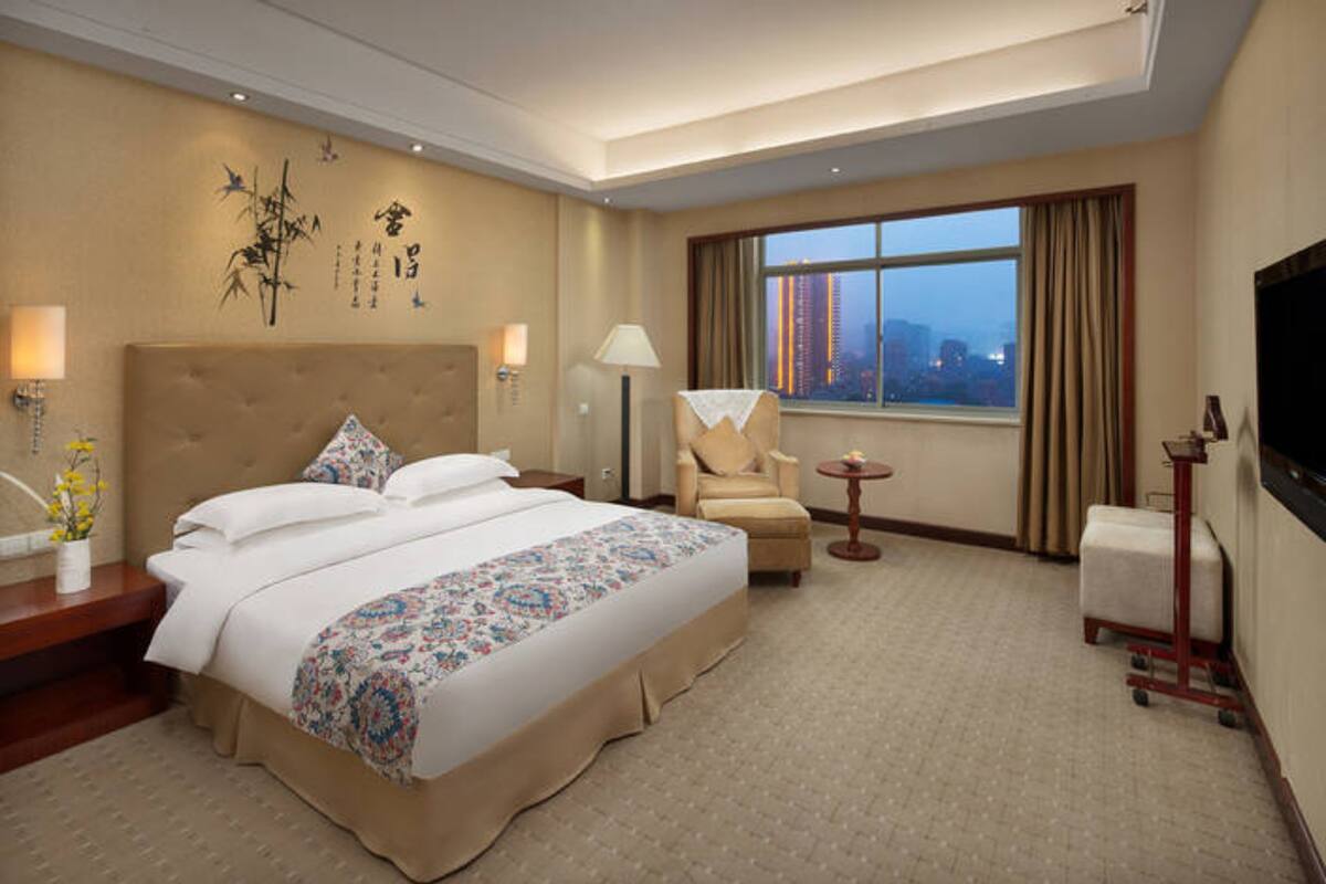 A hotel room with a large bed, a chair, a small table, and a TV.
