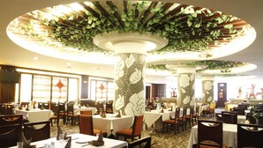 A restaurant with multiple tables and chairs, a patterned floor, and a ceiling with hanging greenery. - Yiyang Huatian Hotel (Yiyang)