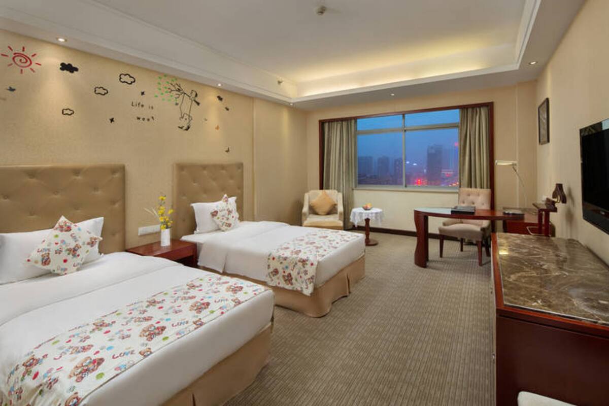 A hotel room with two beds, a desk, a chair, a TV, and a window with a city view.