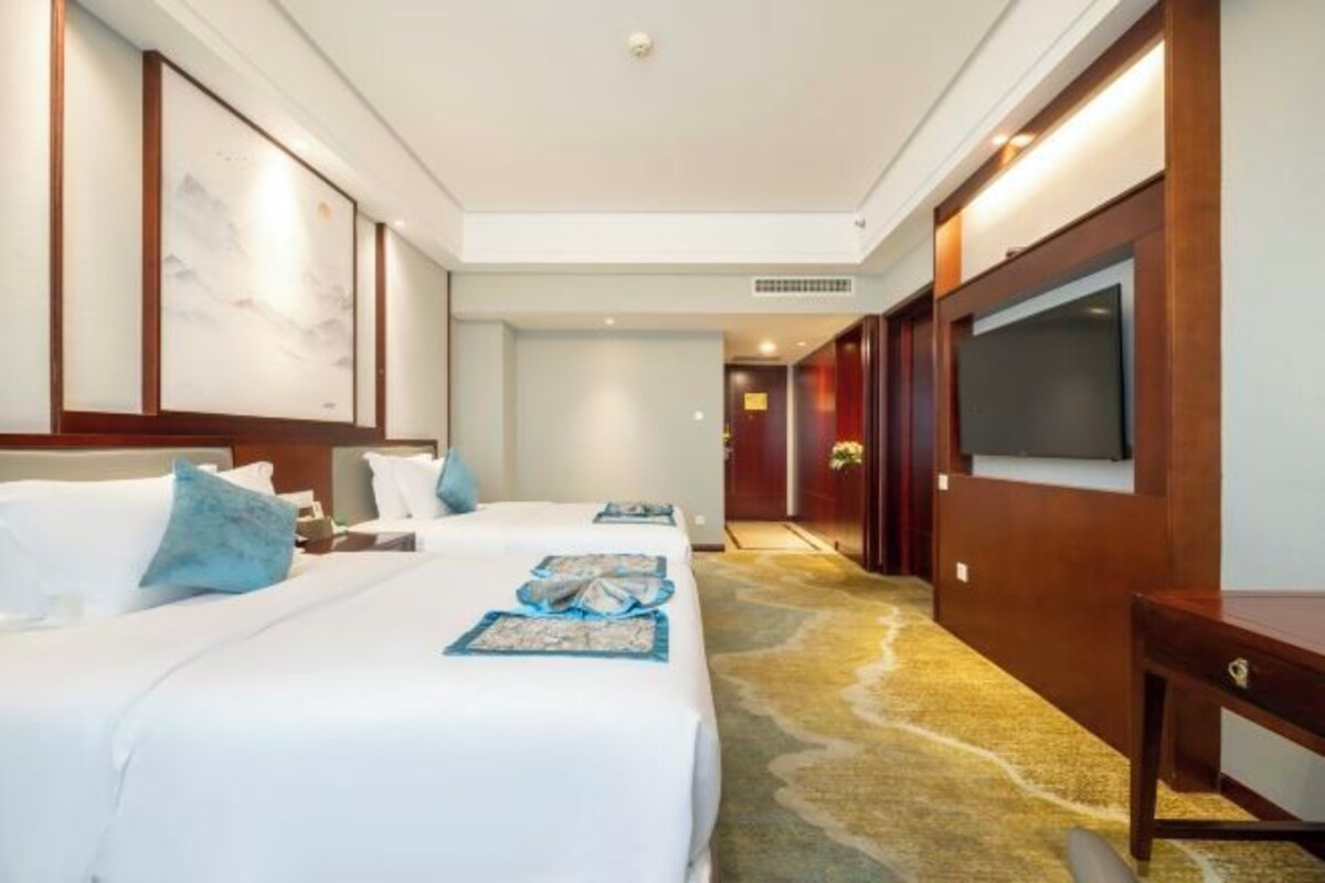 A hotel room with two beds, a TV, and a wooden desk.