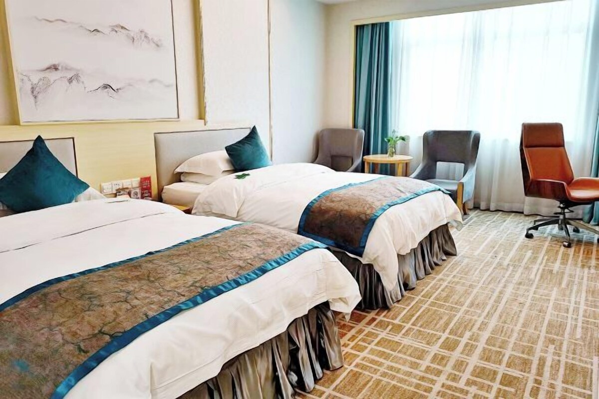 A hotel room with two beds, a desk, a chair, and a large window with curtains.