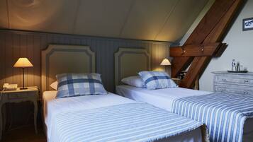 A room with two beds, each with a checkered pillow, a bedside table with a lamp, and a dresser with a small item on top.