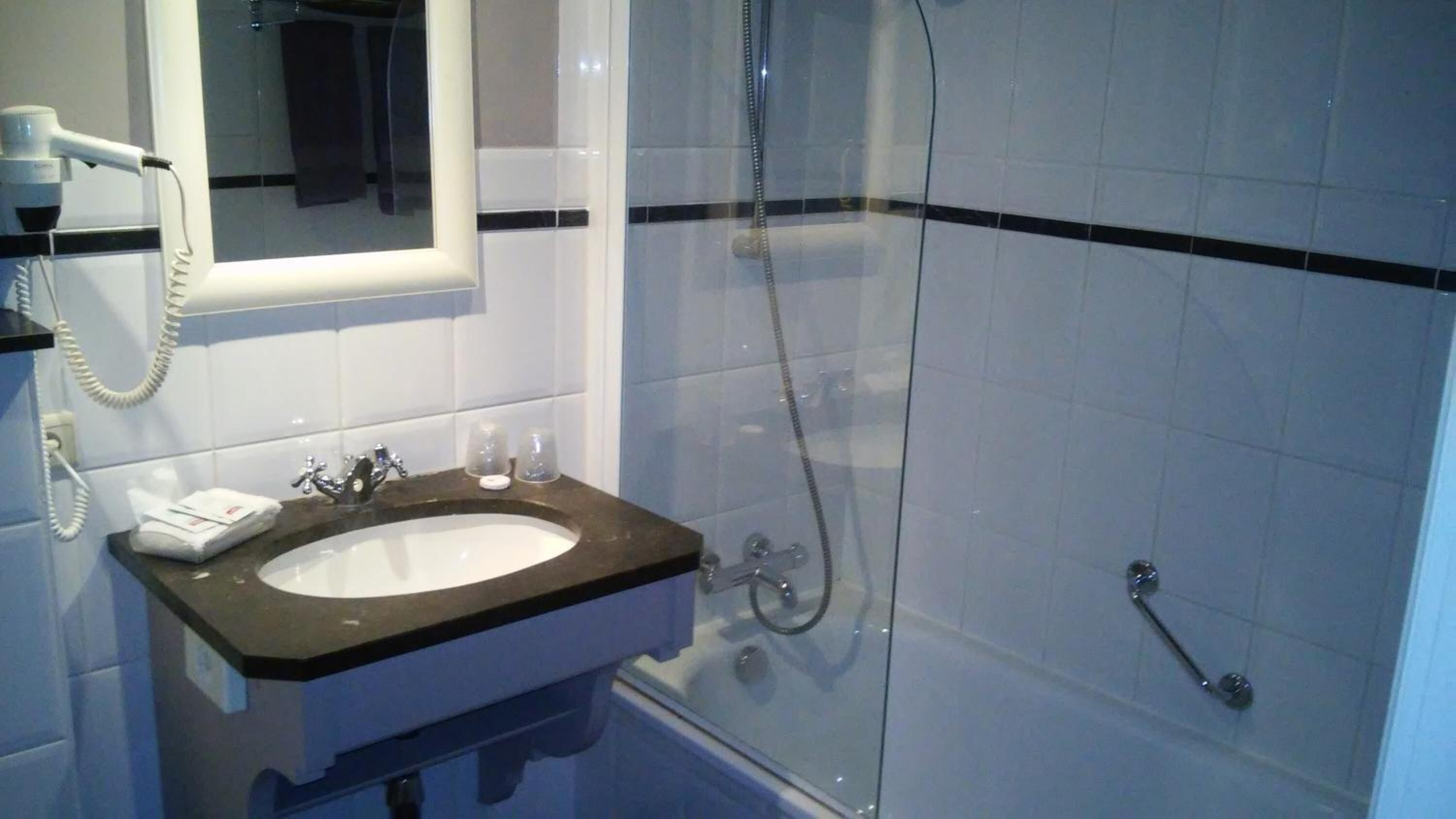 Een badkamer met een wastafel, spiegel, haardroger en douche.