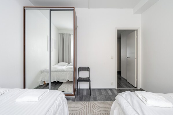 A hotel room with two beds, a mirror, a chair, and a wardrobe.