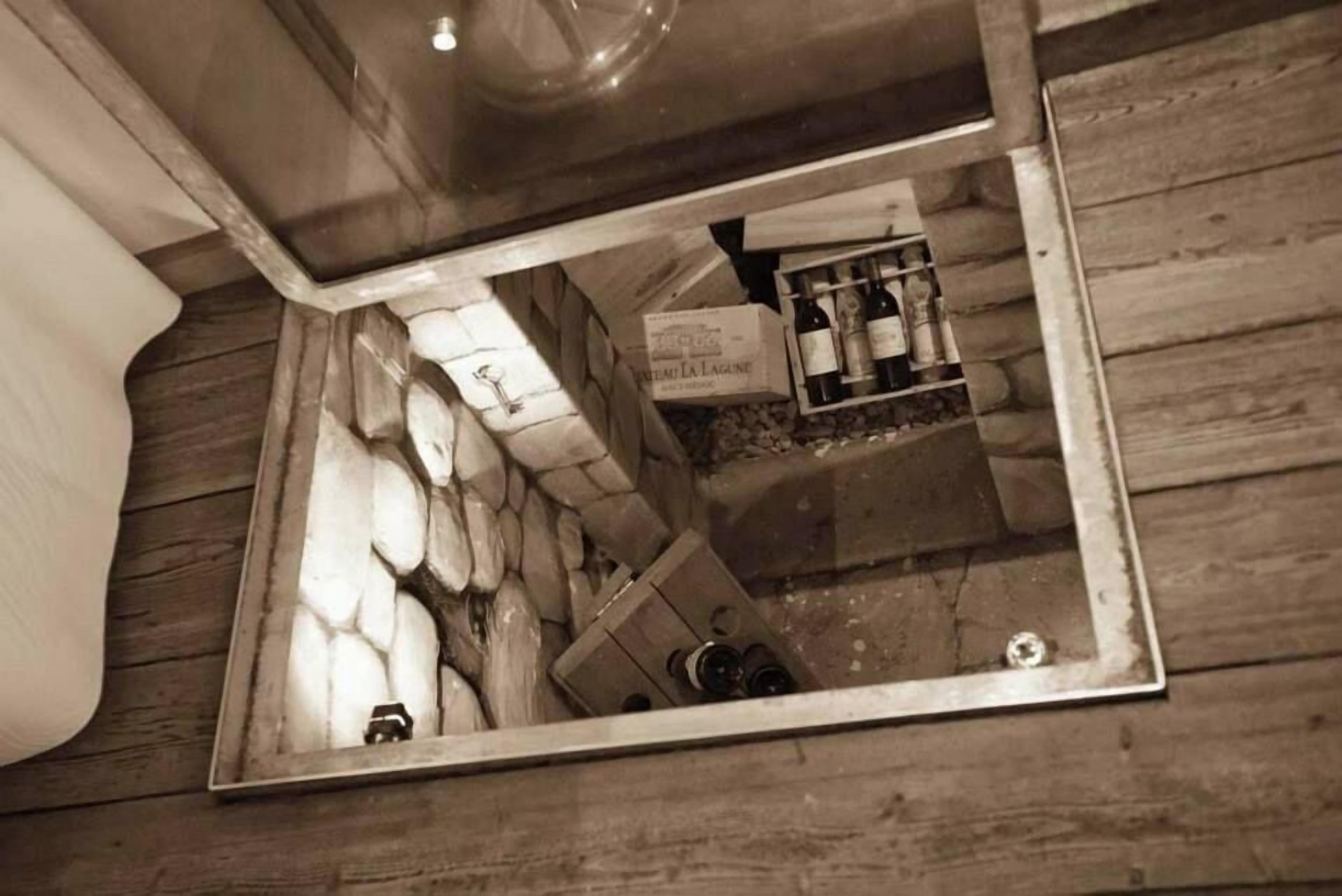 A mirrored view of a room with a wooden floor, a stone wall, and a shelf with bottles.