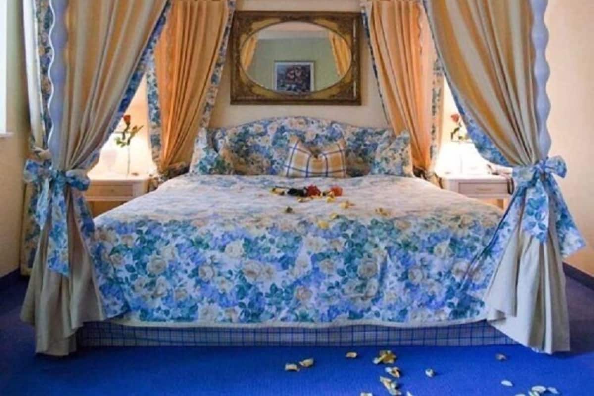 A four-poster canopy bed with floral bedding, a mirror above the bed, and curtains tied at the corners.