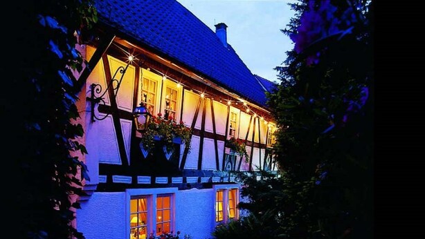 A traditional half-timbered house with illuminated windows and a well-maintained garden. - Landgasthof Alte Bergmühle (Dreieich)