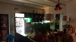 Un área de bar con un refrigerador lleno de bebidas, una barra con plantas en macetas y lámparas colgantes.