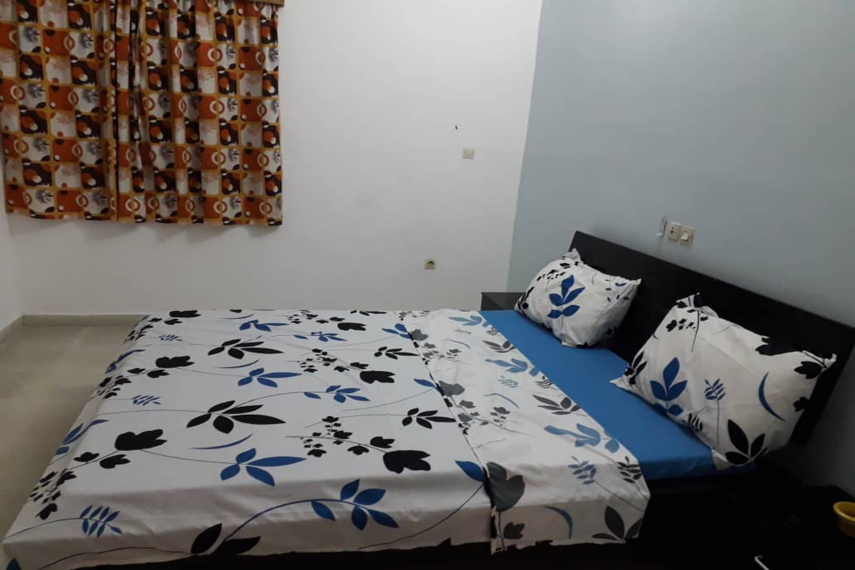 Un dormitorio con cama, edredón y almohadas de estampado floral en azul y blanco.