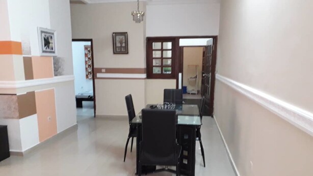 A dining area with a glass table and black chairs, a chandelier, and a door leading to another room. - Peniel Residence (Abidjan)