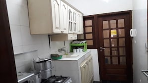 A compact kitchen with white cabinets, a stove, and a sink. - Peniel Residence (Abidjan)
