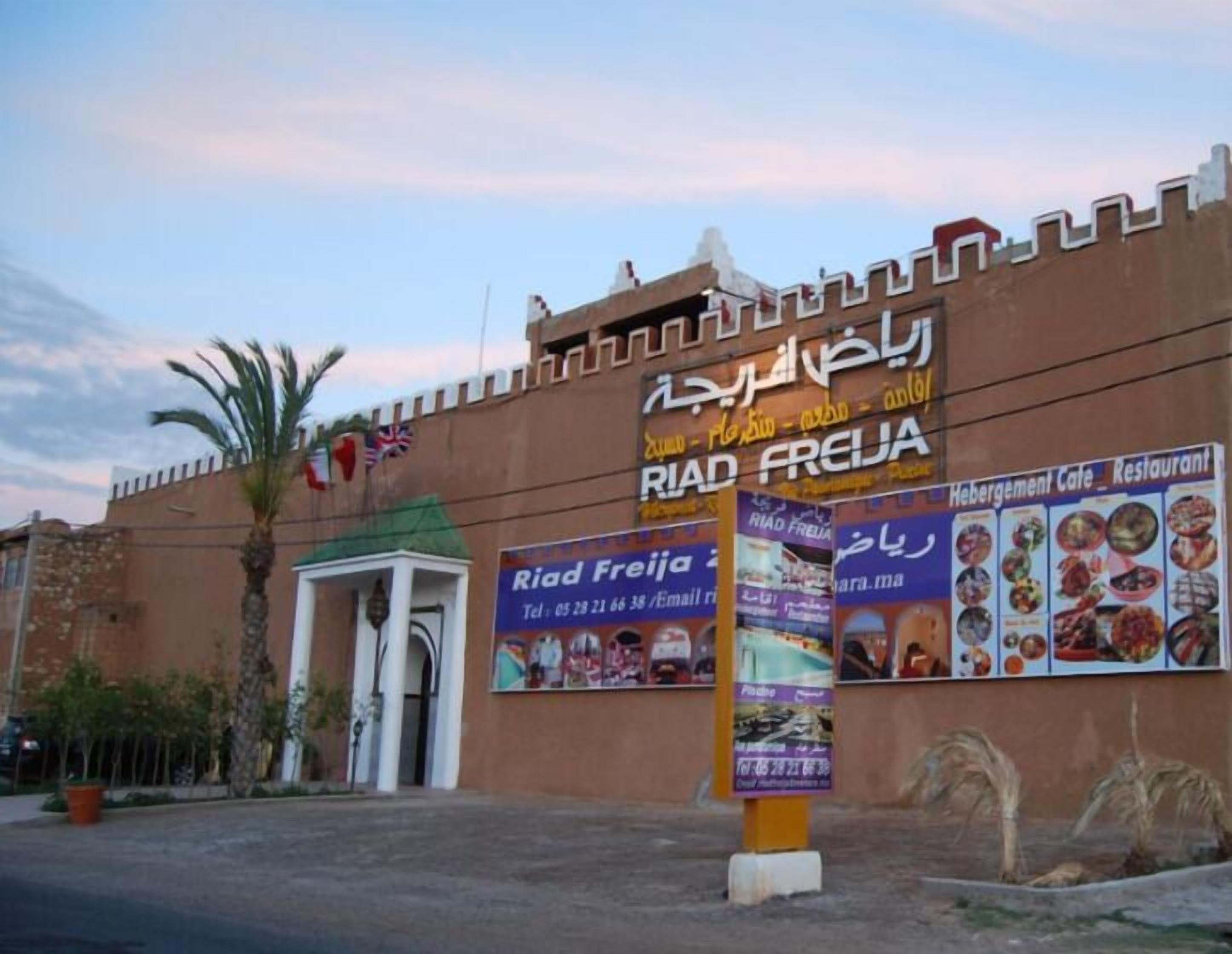 Un bâtiment portant une enseigne « Riad Freija » et un panneau affichant un menu pour un « Café-restaurant proposant des hébergements ».