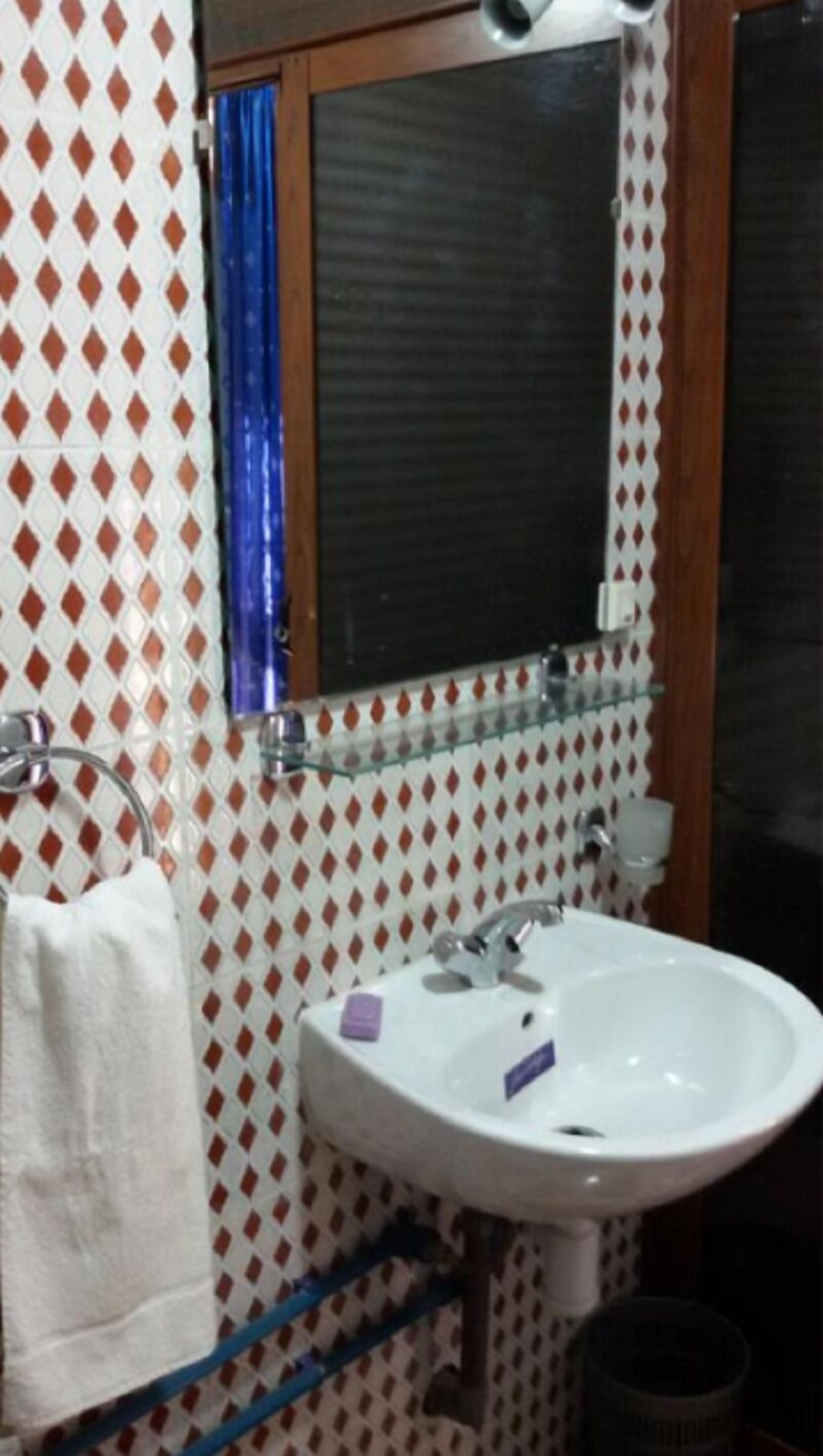 A bathroom with a white sink, a mirror, and a patterned wall.
