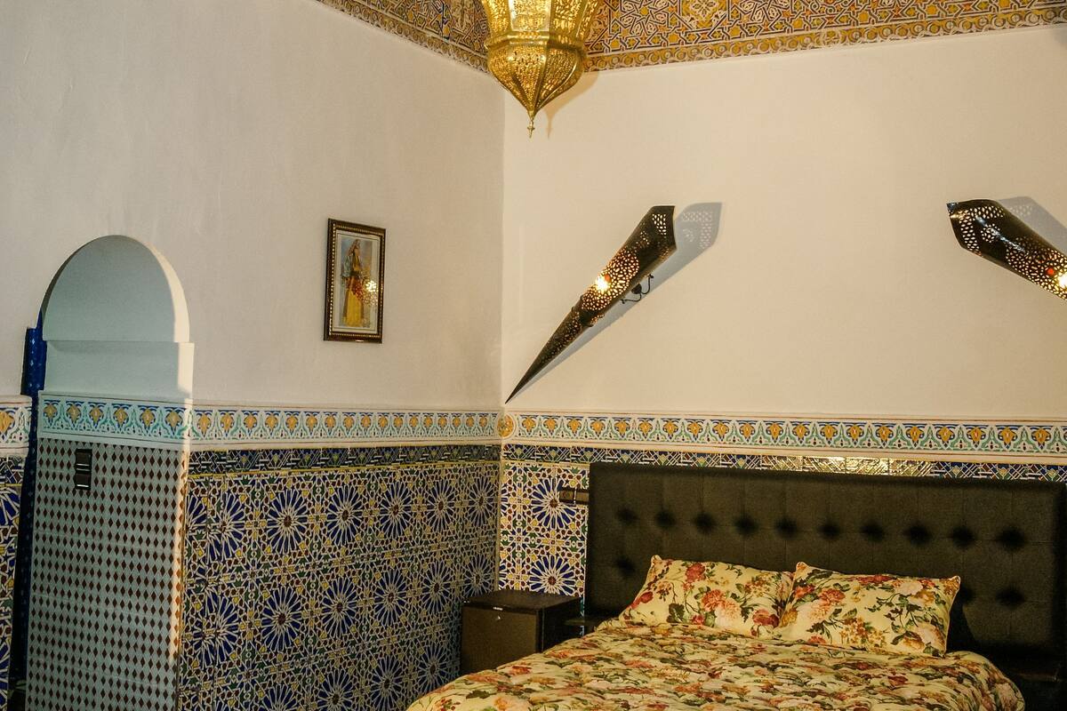 Una habitación con una cama, un candelabro, paredes con diseño y suelo a cuadros.
