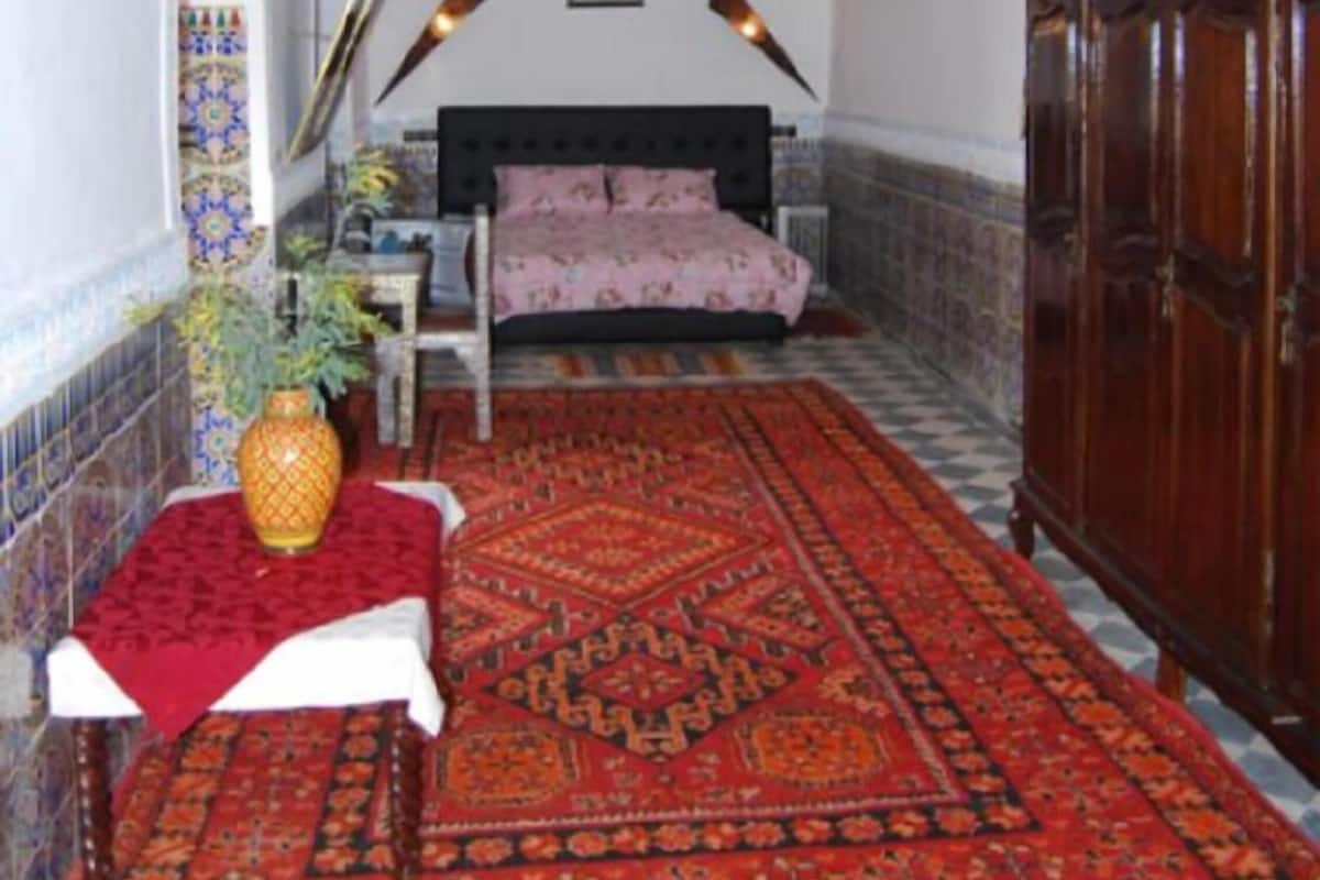 Una habitación con una cama, un armario de madera, un tapete estampado y faroles colgantes.