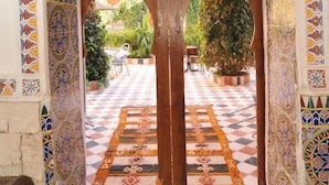 An ornate doorway with intricate tile work, leading to a courtyard with a checkered floor and potted plants. - Riad Freija (Freyja)