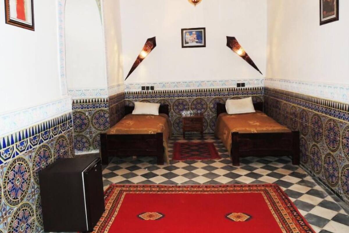 Una habitación con dos camas, alfombra roja, paredes con diseño y una lámpara colgante.
